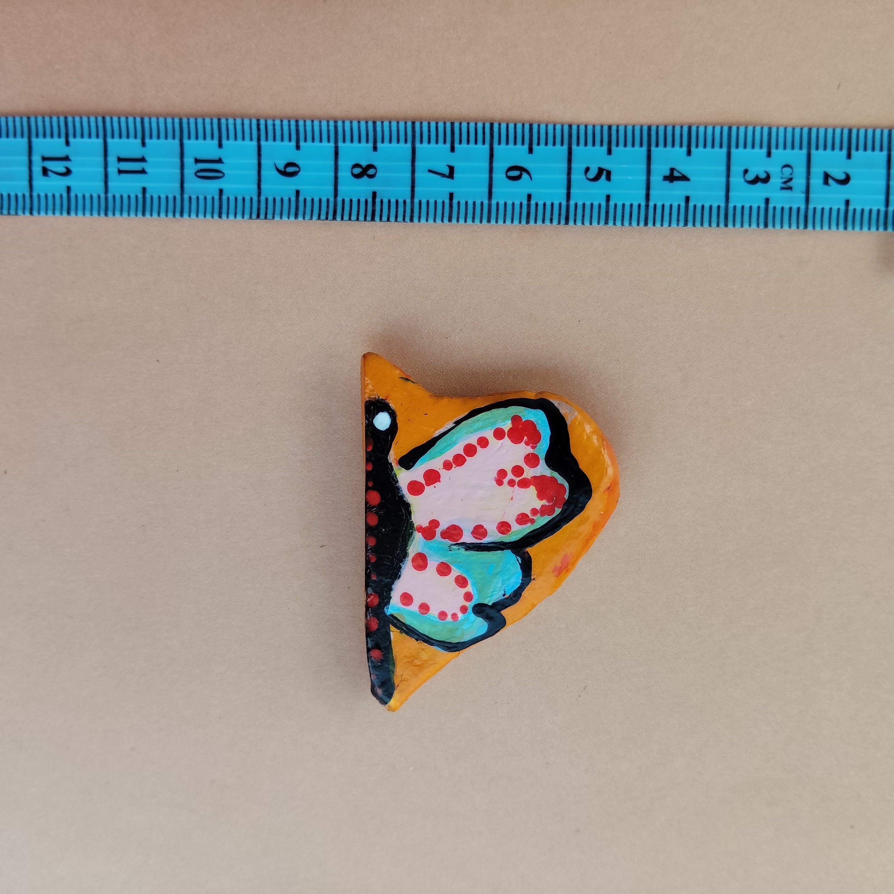 Colorful butterfly-shaped object next to a blue measuring tape on a beige background - Sustainable Home Decor & Upcycled Glass