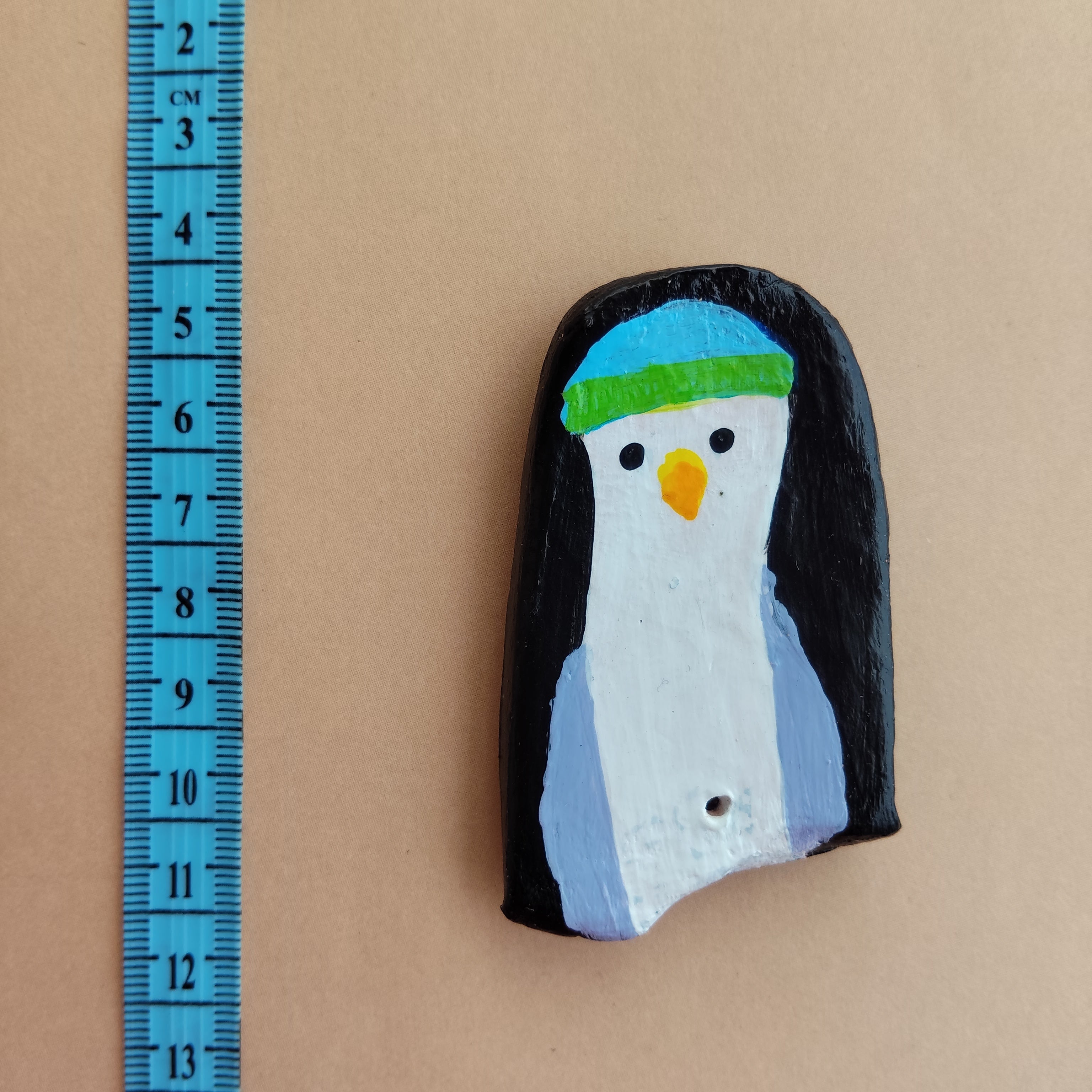 Penguin-shaped handmade magnet with a colorful design on a beige background, measured by a blue ruler. - Sustainable Home Decor & Upcycled Glass