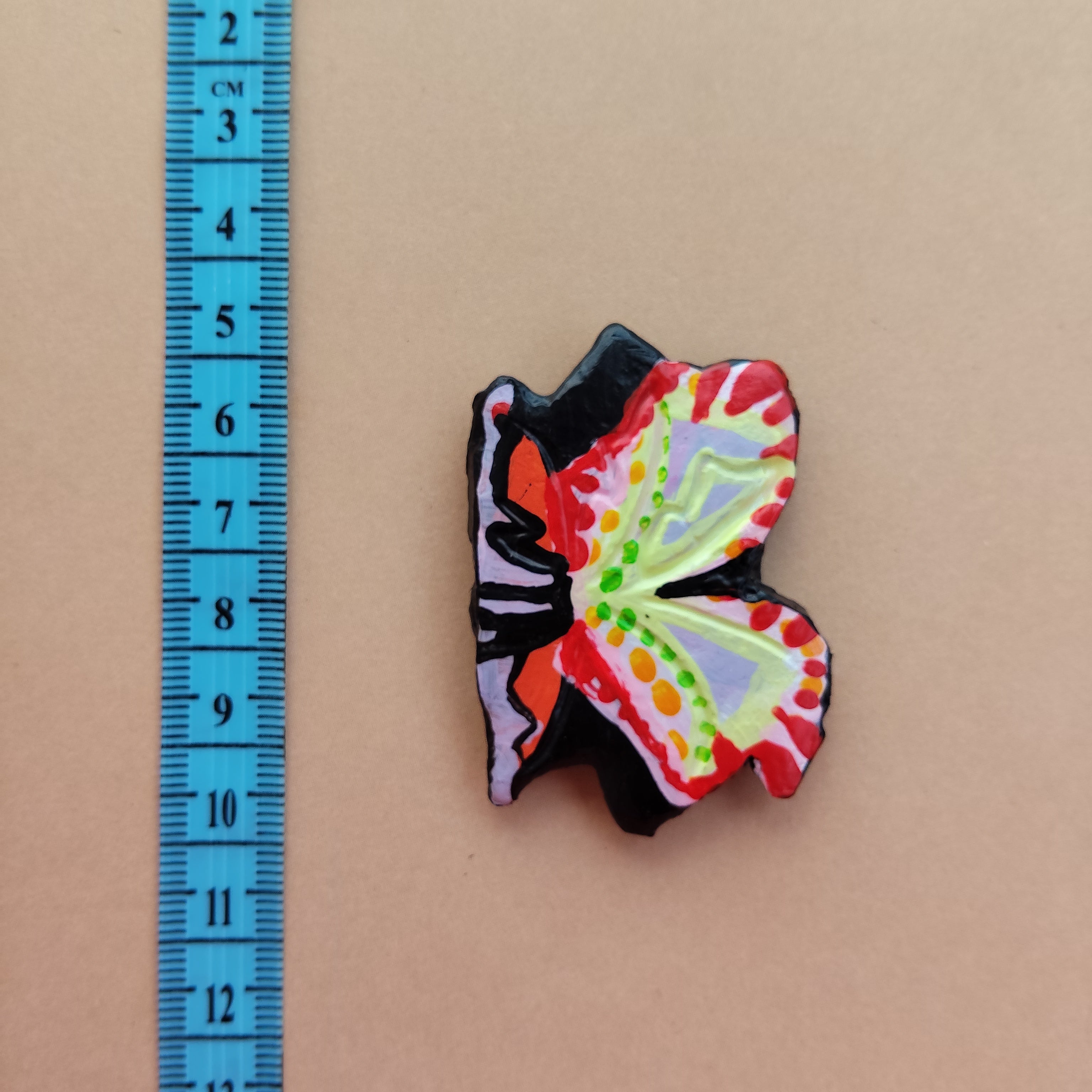 Colorful butterfly-shaped object next to a ruler on a beige background - Sustainable Home Decor & Upcycled Glass