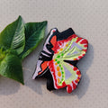 Colorful butterfly-shaped object on a textured surface with green leaves.