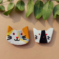 Two cat figures on a beige background with green leaves.