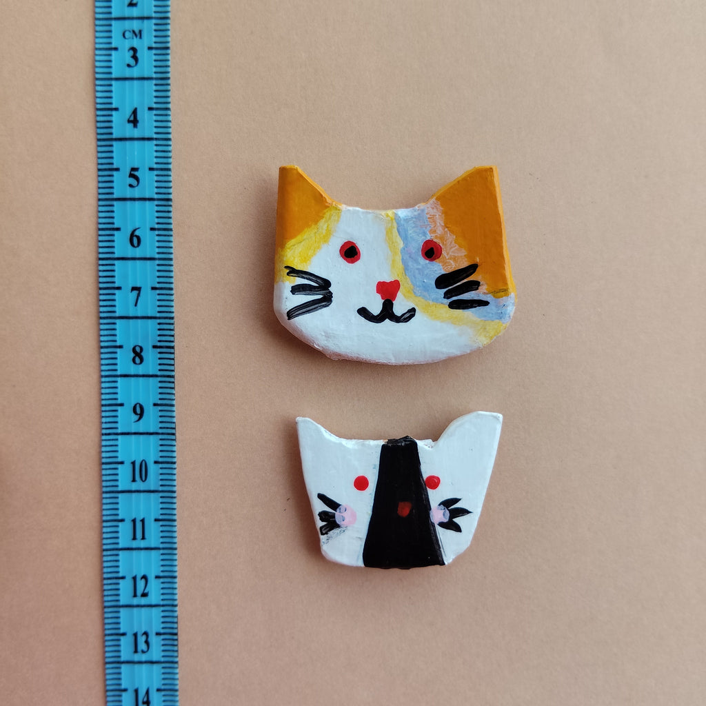 Two handmade cat face with artistic designs on a beige background, accompanied by a blue ruler for scale. - Sustainable Home Decor