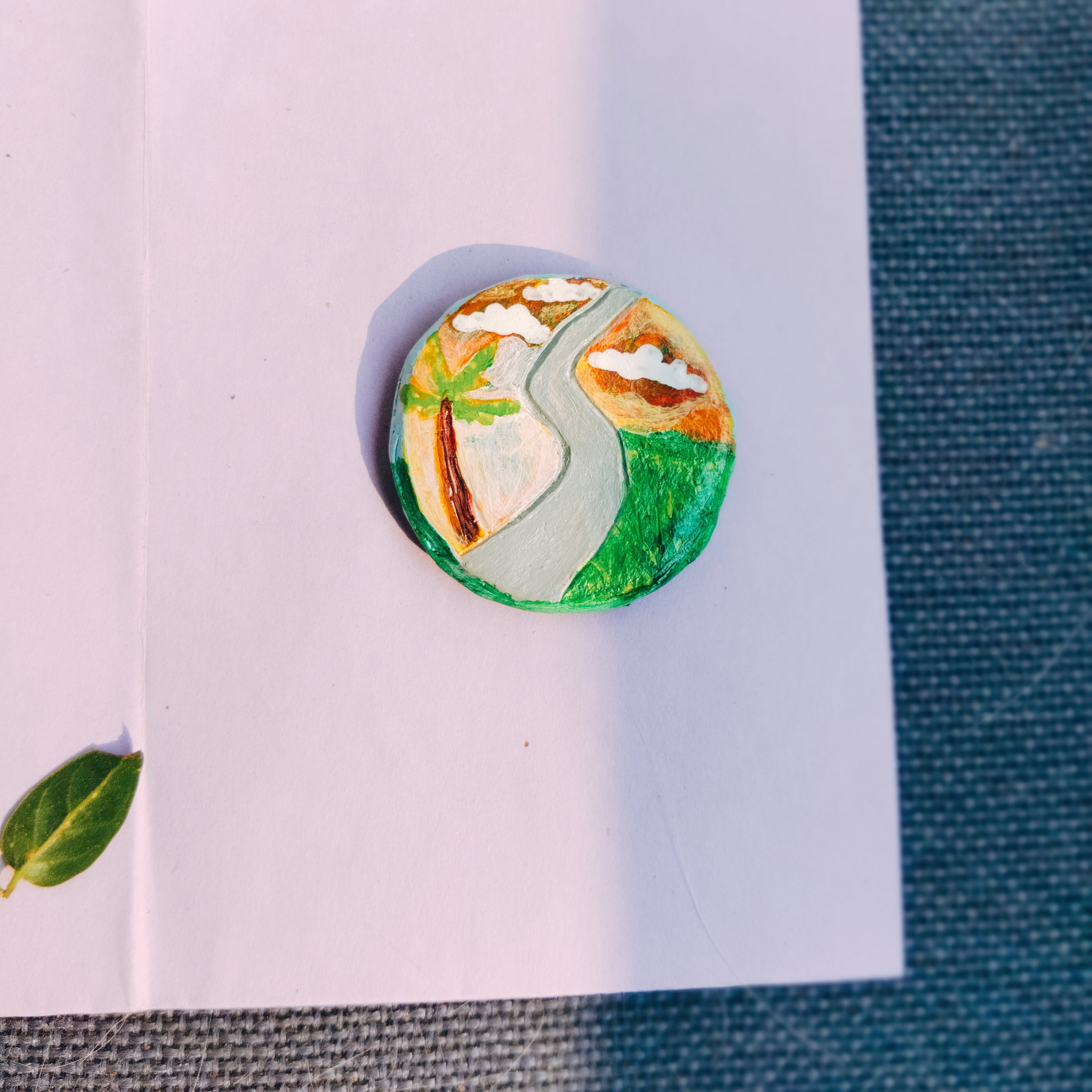 Round planet-friendly fridge magnet with nature-themed design with palm tree, narrow lanes in a sunset background.