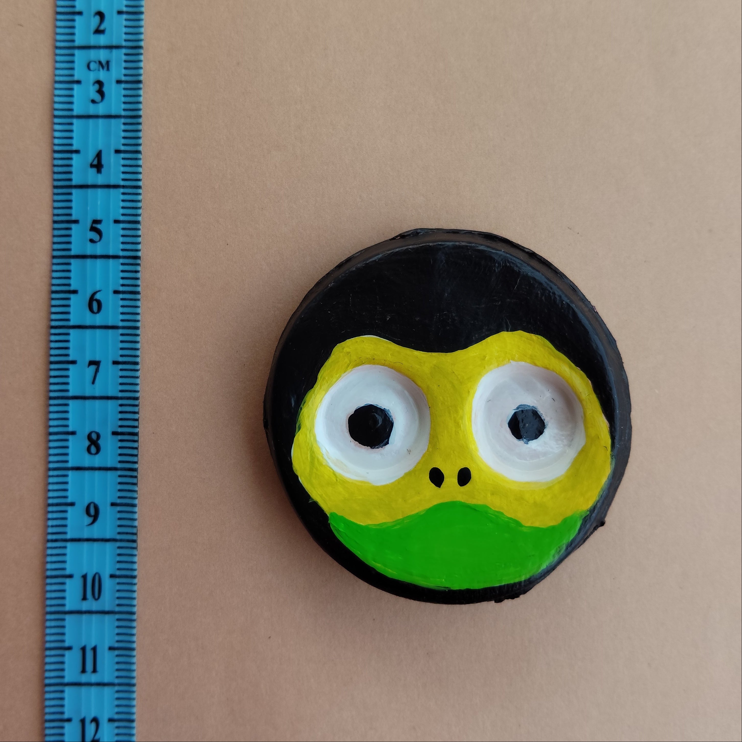 Round object with a frog face design on a beige surface with a blue ruler for scale. - Sustainable Home Decor & Upcycled Glass
