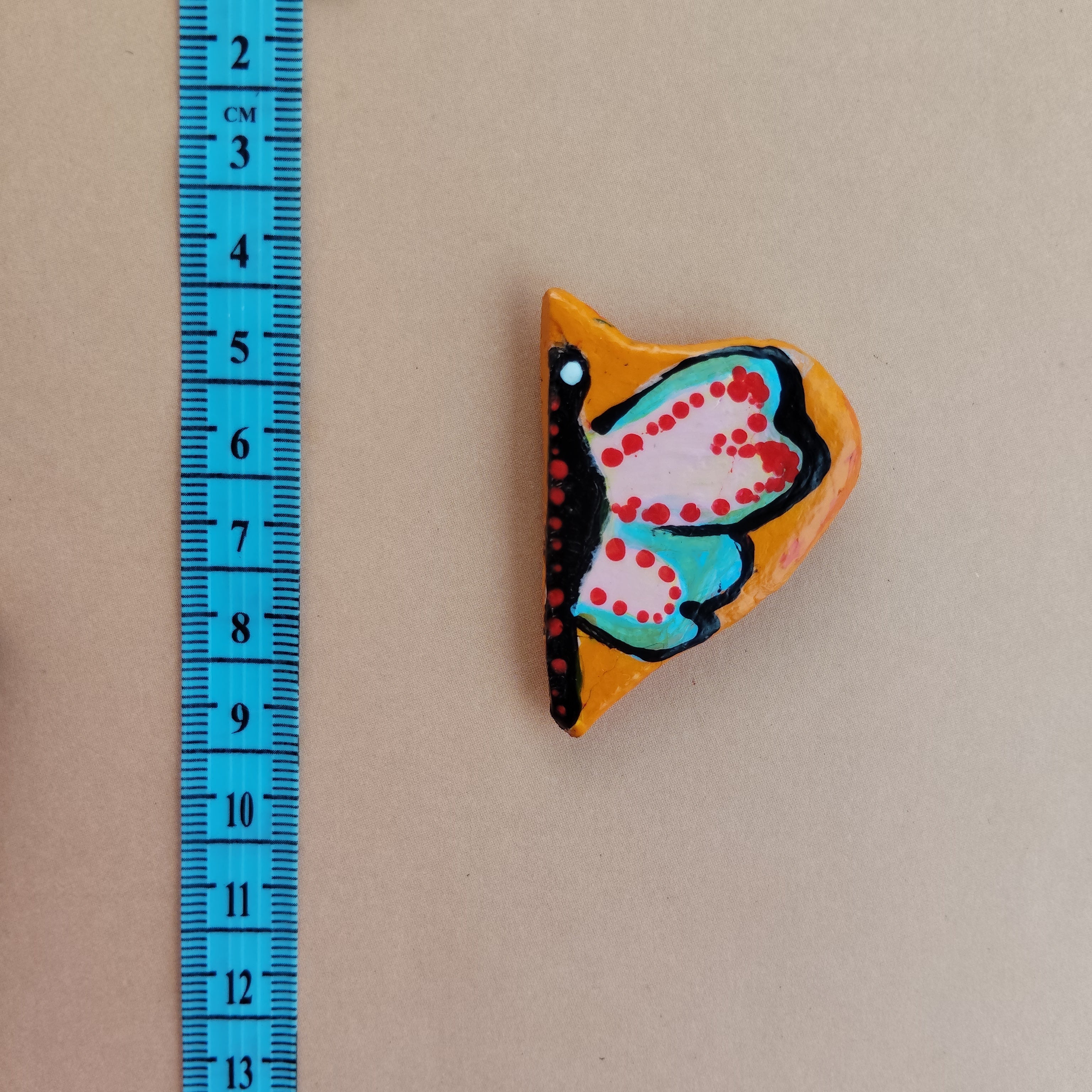 Colorful butterfly-shaped object next to a blue measuring tape on a beige background. - Sustainable Home Decor & Upcycled Glass