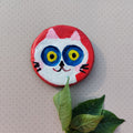 Colorful white cat-shaped magnet with leaves on a textured beige background
