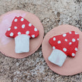 Two red mushroom-shaped magnets with white dots on a pink base on a textured surface.