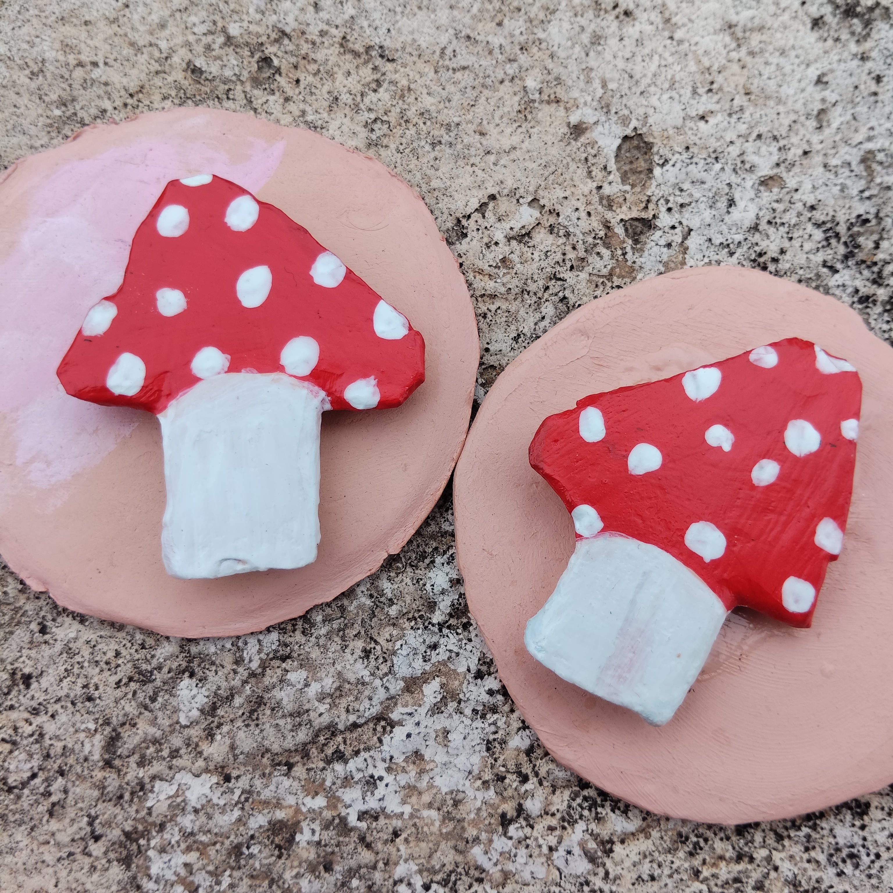 Two red mushroom-shaped magnets with white dots on a pink base on a textured surface. - Sustainable Home Decor & Upcycled Glass