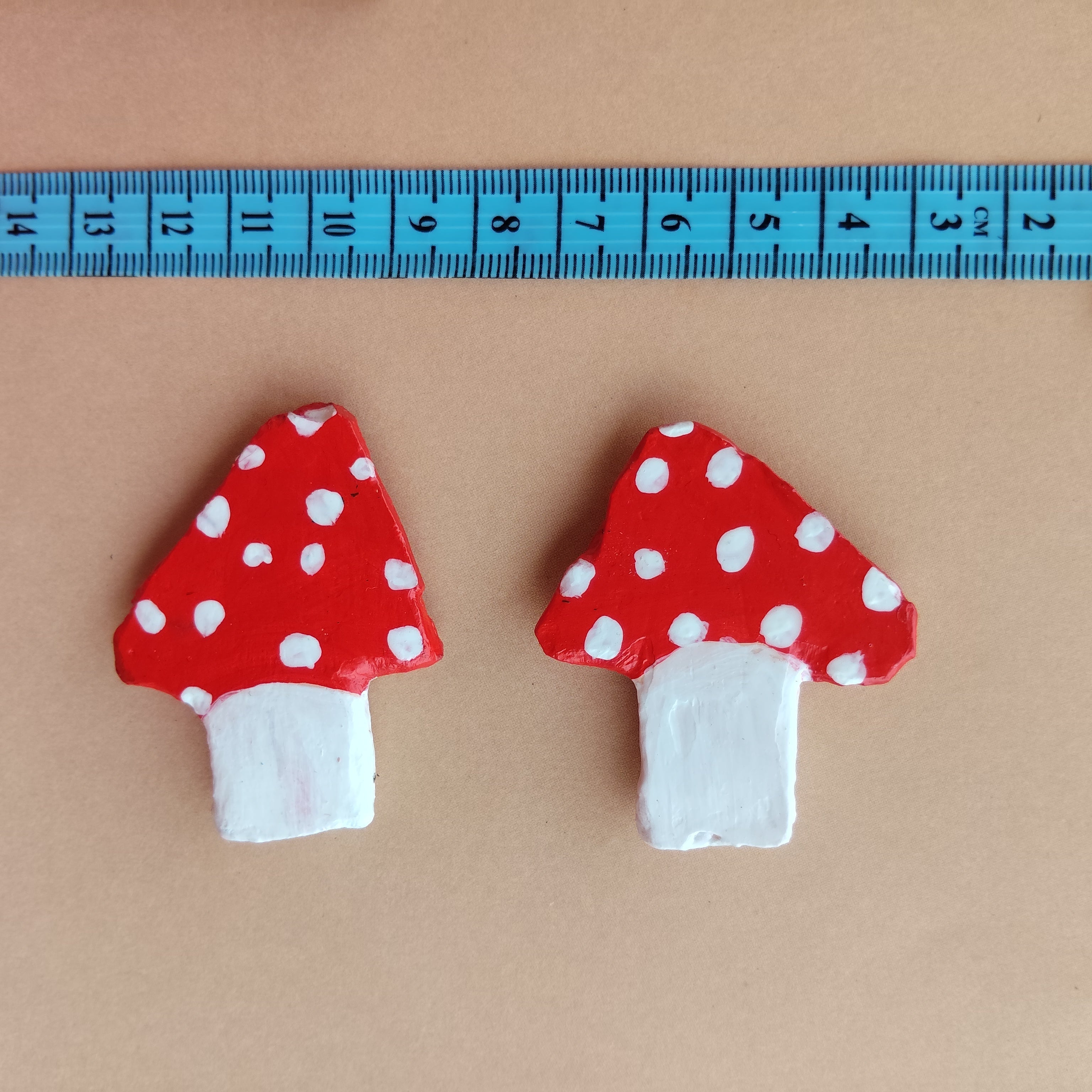 Two red mushroom-shaped art with white polka dots on a beige background, measured by a blue ruler. - Sustainable Home Decor & Upcycled Glass