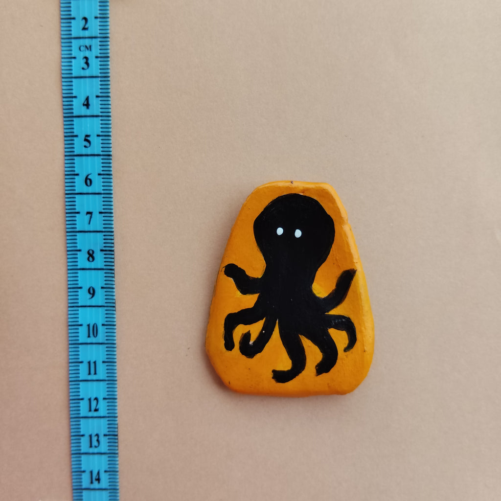 Black octopus design on a yellow hand-crafted magnet with a blue ruler for scale on a beige background - Sustainable Home Decor