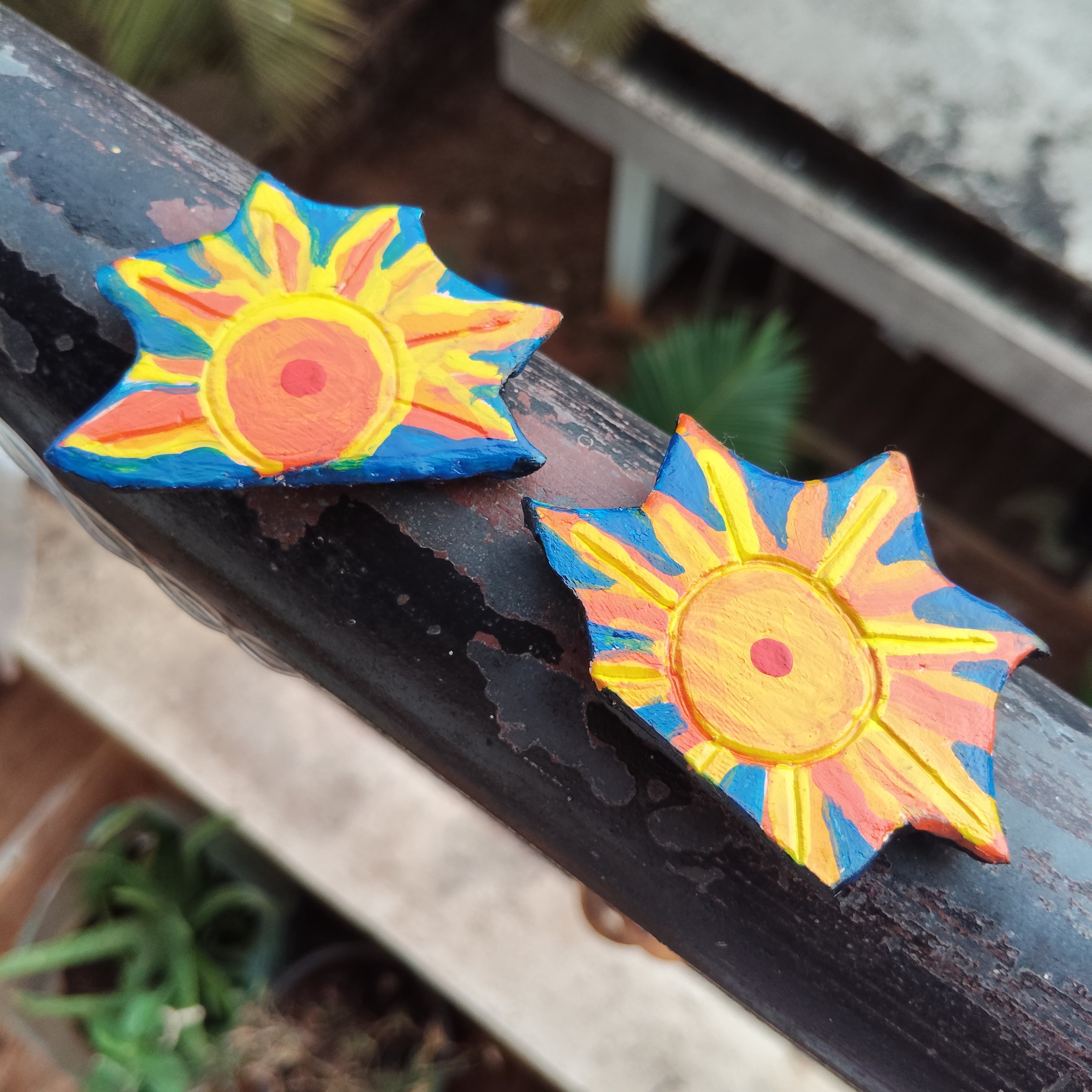 Colorful sun-shaped magnet duo on a dark surface with a blurred naturistic background. - Sustainable Home Decor & Upcycled Glass