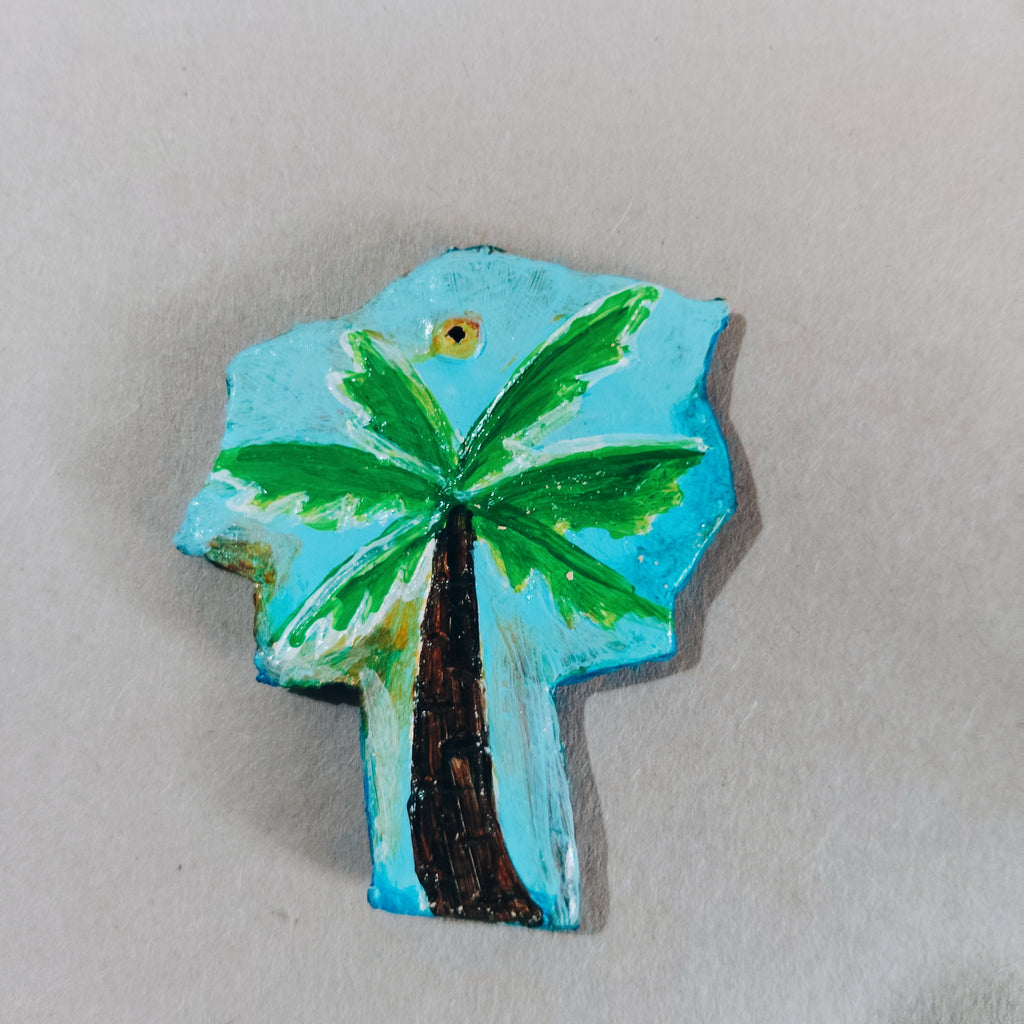 Palm tree design hand-painted sustainable with a blue background on a clay surface. Its from eco friendly magnets collection of kalakarwaa