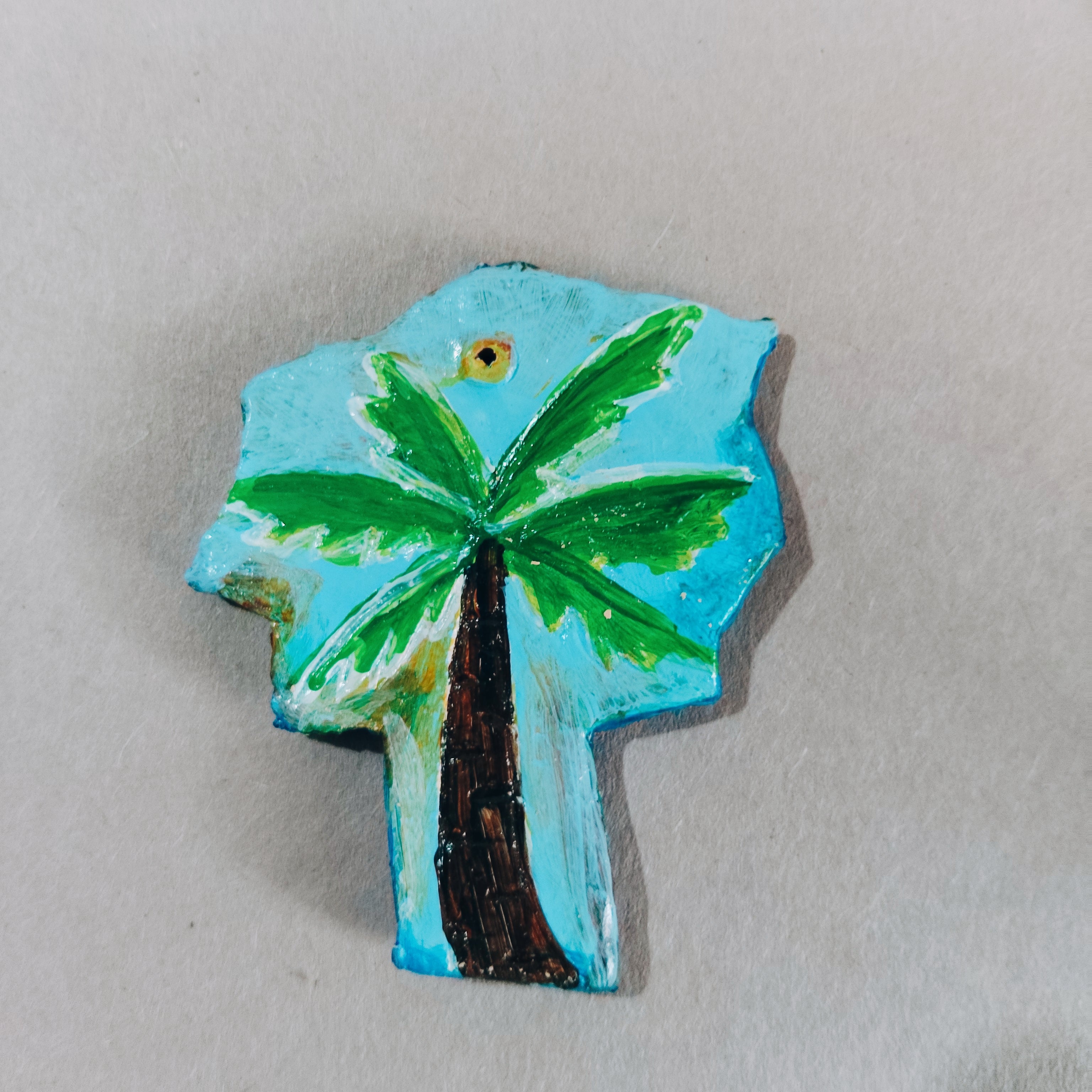 Palm tree design hand-painted sustainable with a blue background on a clay surface. Its from eco friendly magnets collection of kalakarwaa