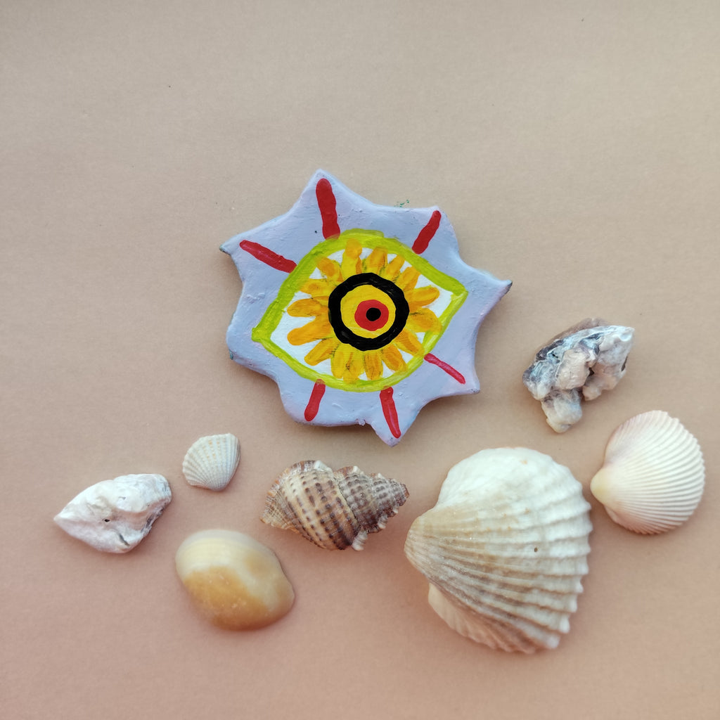 Artistic magnet with a colorful design surrounded by various shells on a beige background. - Sustainable Home Decor