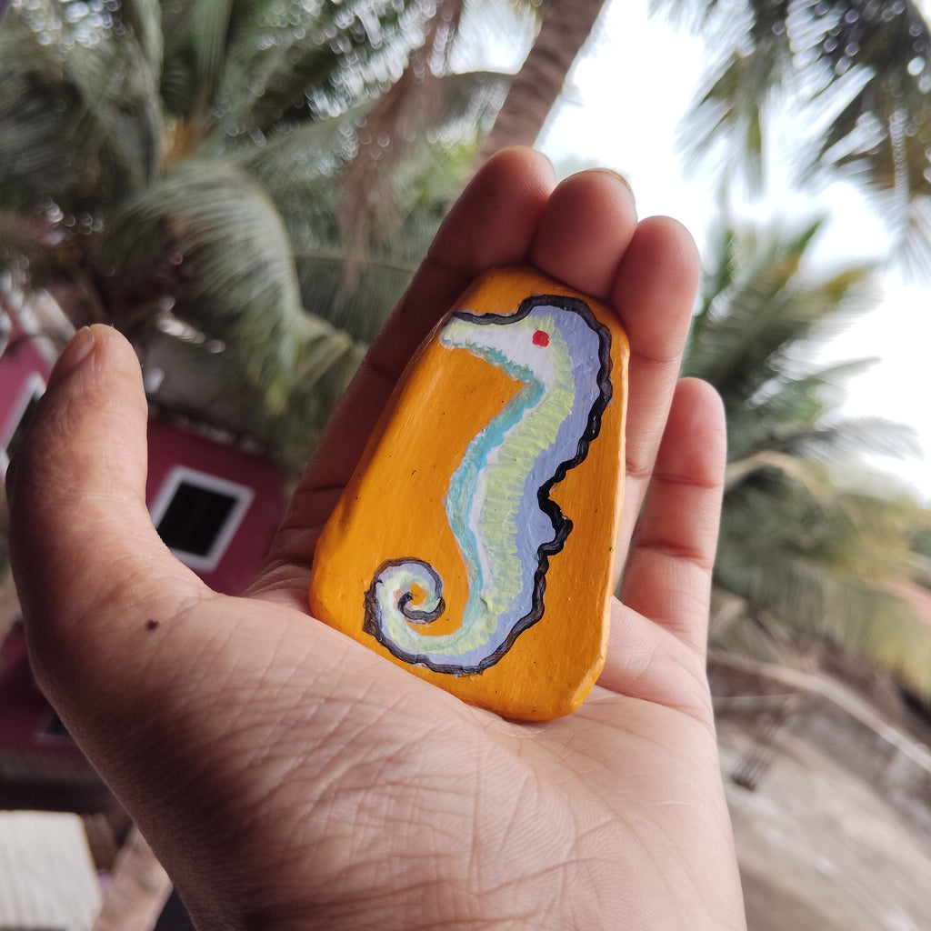 Hand holding a painted magnet with a seahorse design against a blurred natural background. - Sustainable Home Decor
