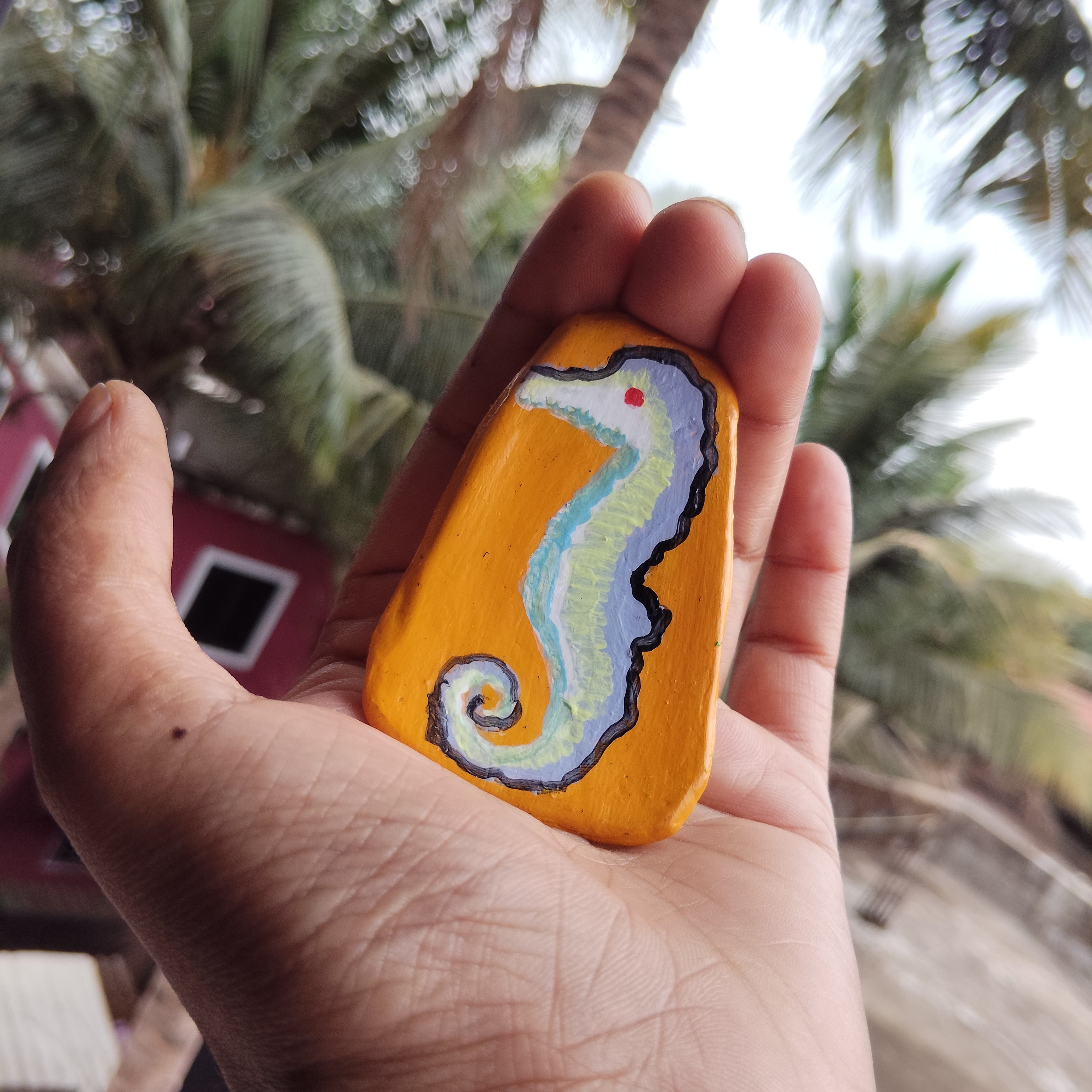 Hand holding a painted magnet with a seahorse design against a blurred natural background. - Sustainable Home Decor & Upcycled Glass