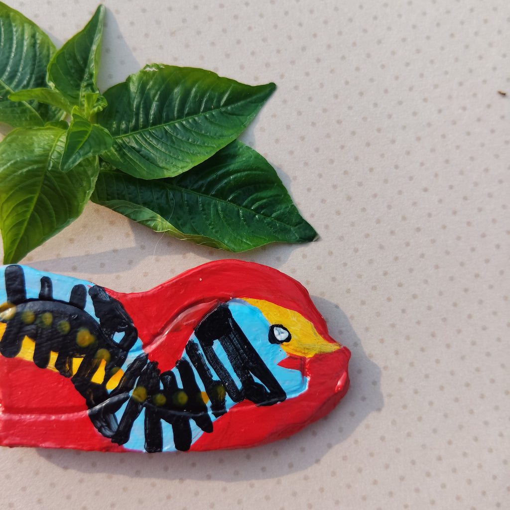 Colorful snake-shaped magnet with black and yellow design on a textured surface with green leaves. - Sustainable Home Decor