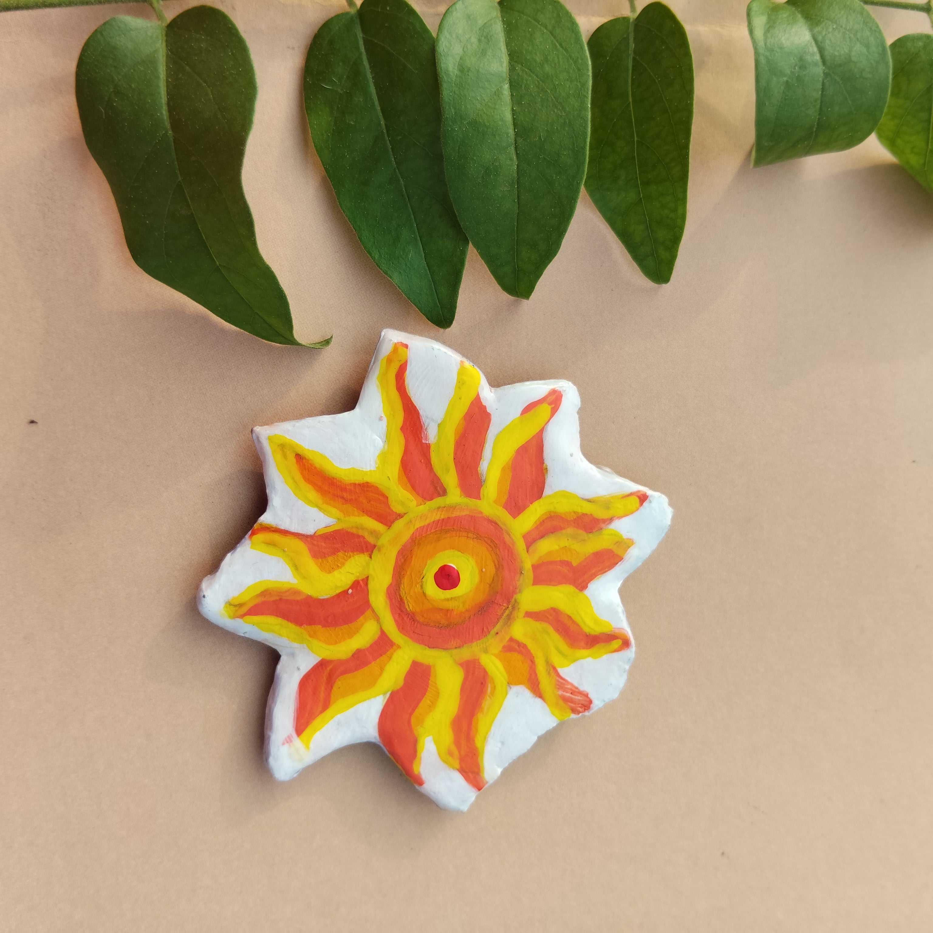 Colorful sun-shaped object on a beige background with green leaves - Sustainable Home Decor & Upcycled Glass