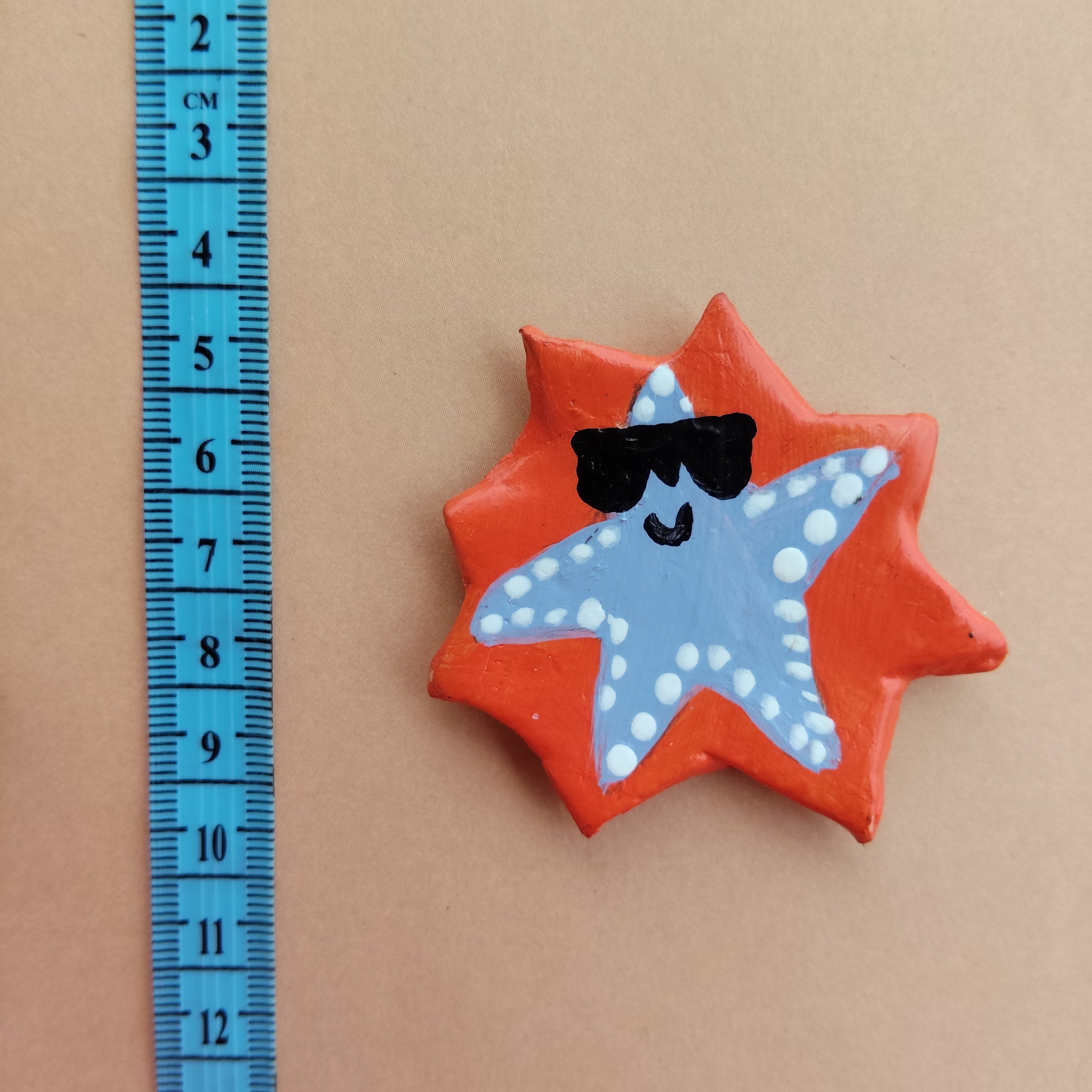 Star-shaped magnet with orange border and greyish blue center featuring a starfish, next to a blue ruler for scale on a beige background. - Sustainable Home Decor & Upcycled Glass