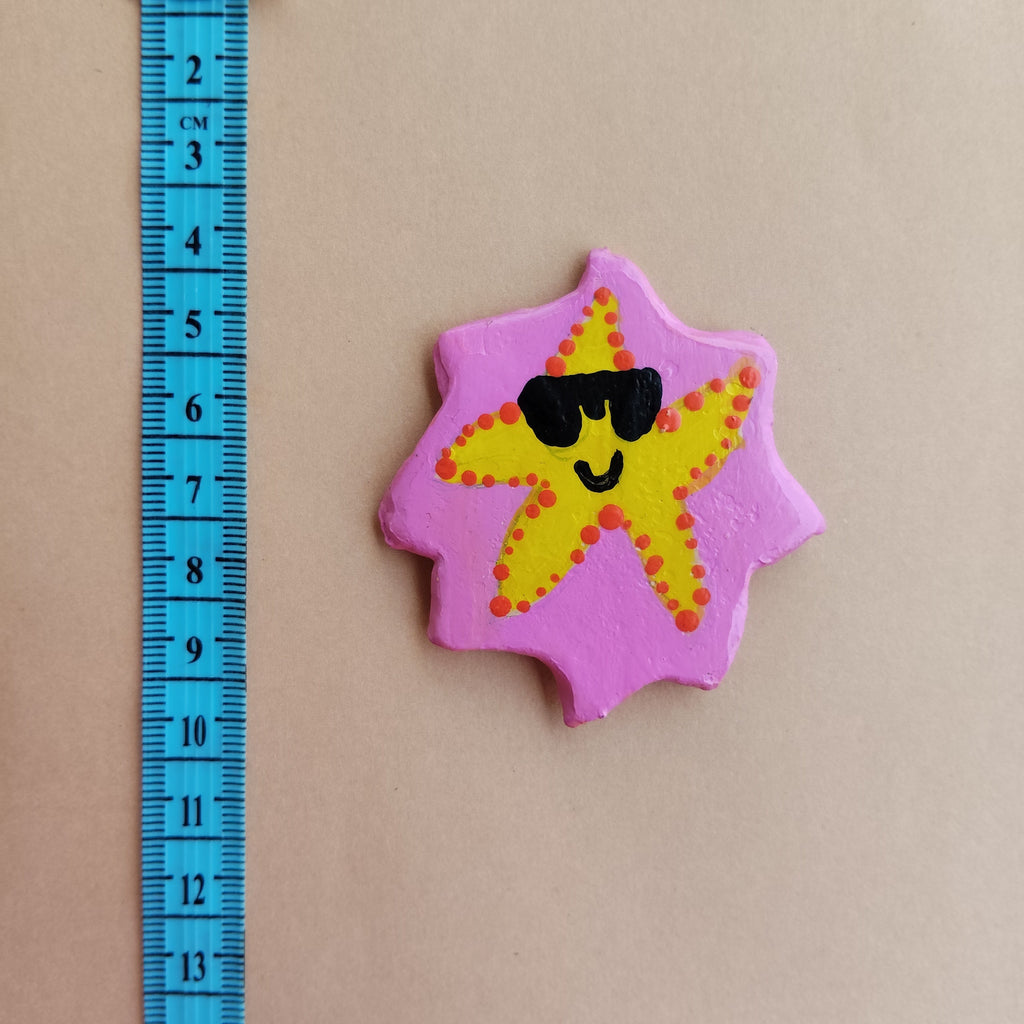 Star-shaped magnet with a face design on a beige background, measured by a blue ruler. - Sustainable Home Decor