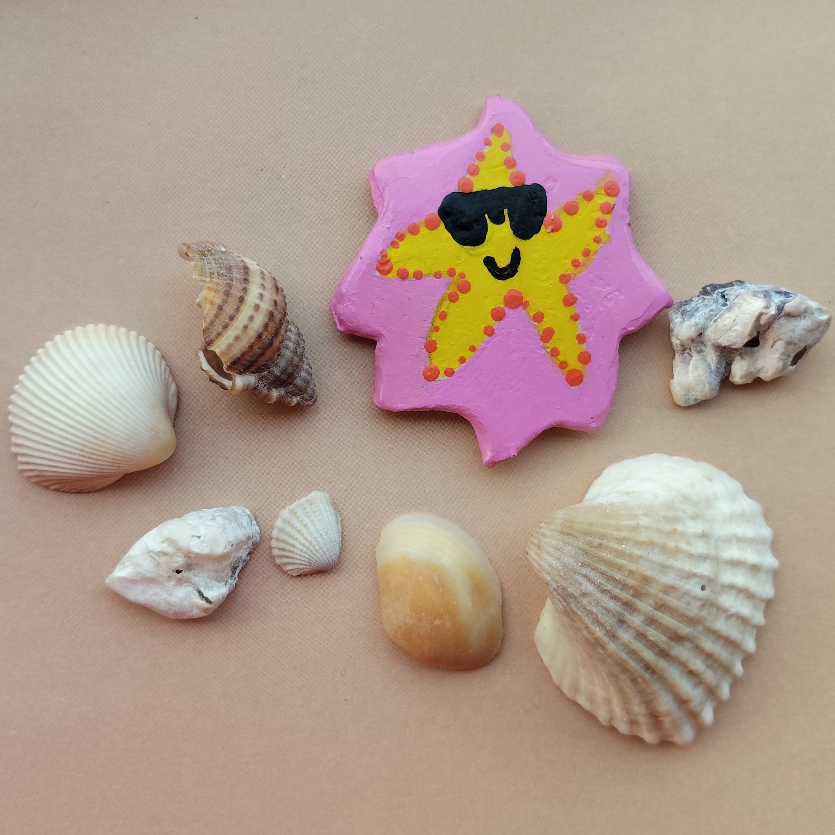 Decorative starfish with sunglasses on a pink hand-crafted magnet, lying on beige background, surrounded by real shells. - Sustainable Home Decor & Upcycled Glass