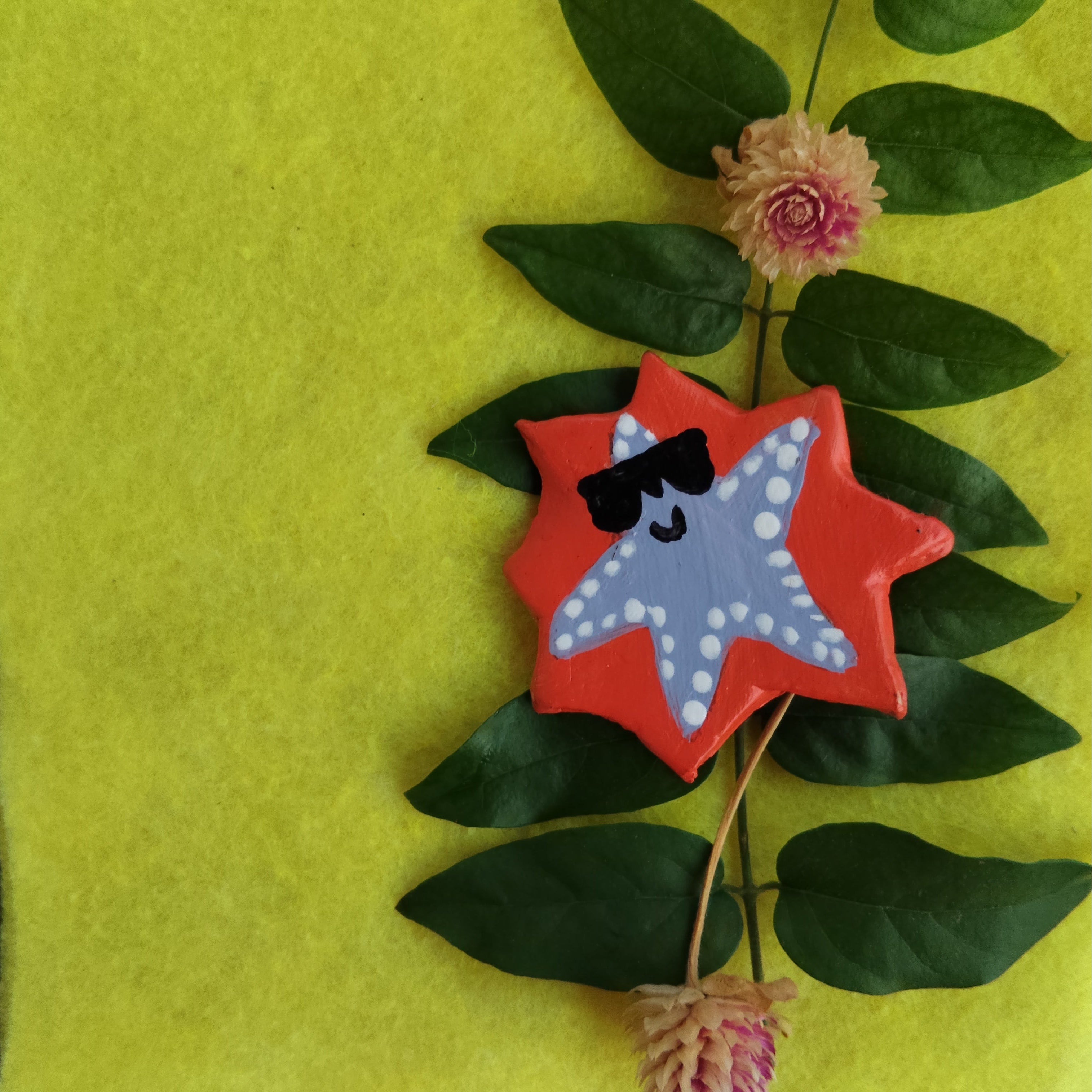 Star-shaped object with a face lying on green leaves and flowers - Sustainable Home Decor & Upcycled Glass