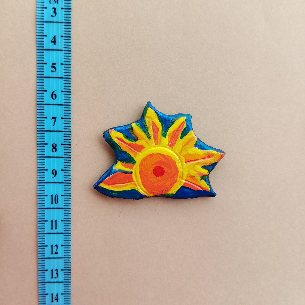 Colorful sun-shaped hand-painted magnet next to a ruler on a beige background. - Sustainable Home Decor