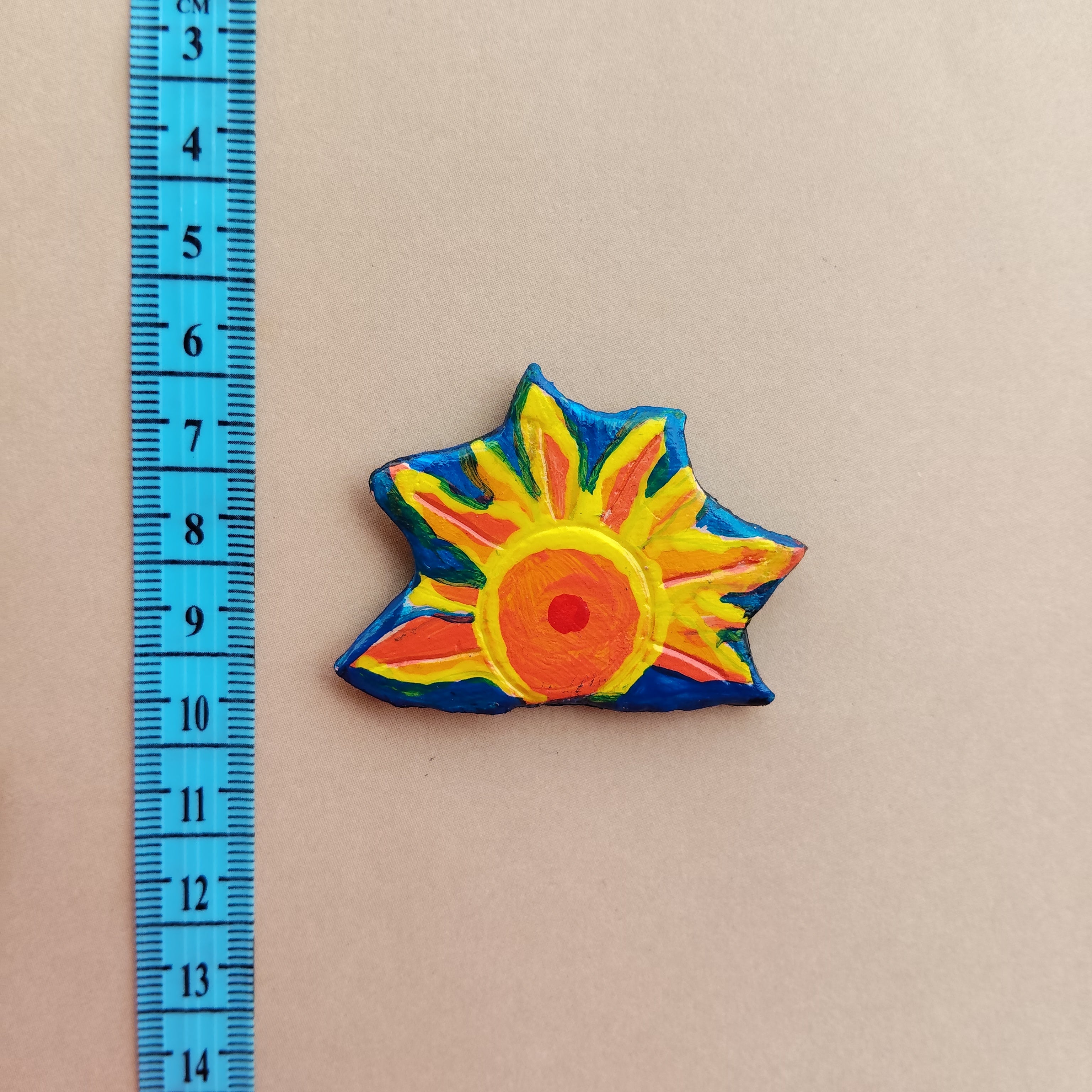 Colorful sun-shaped hand-painted magnet next to a ruler on a beige background. - Sustainable Home Decor & Upcycled Glass