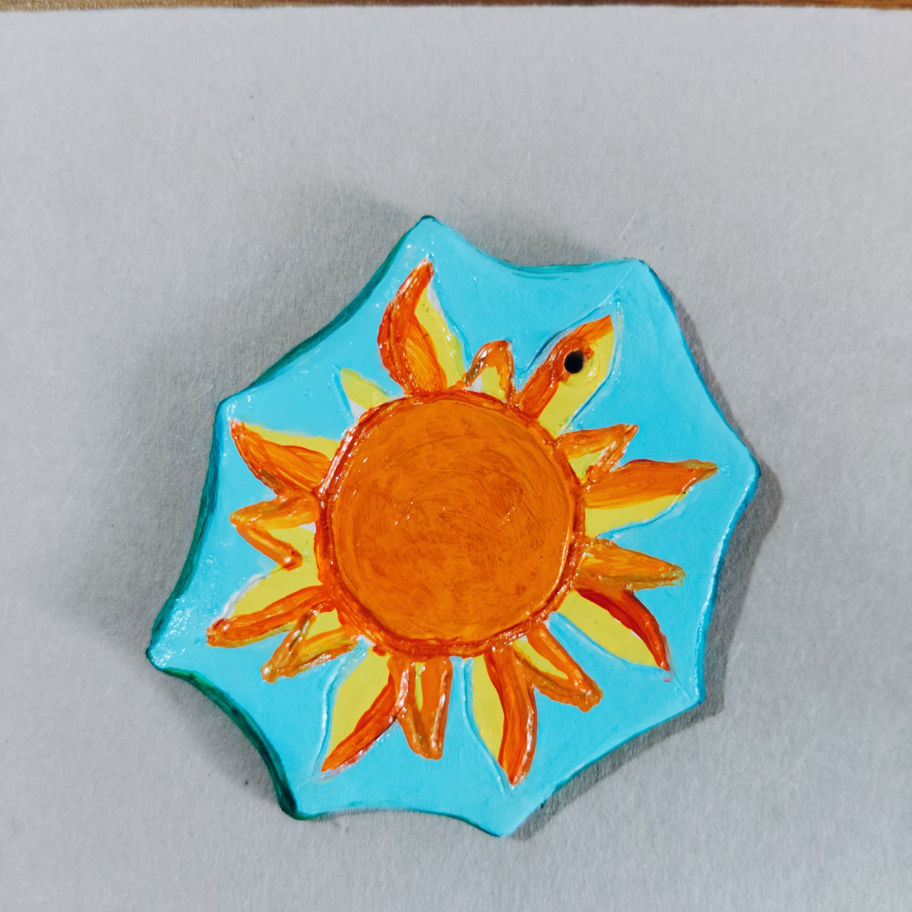 Hand-crafted fridge magnet with a sun design on a light blue background.