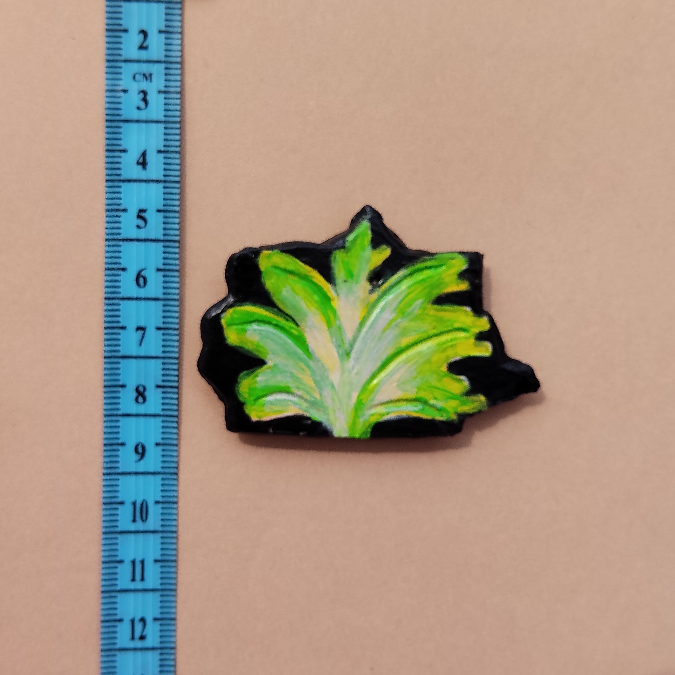 Green leaf-shaped hand-crafted magnet on a beige surface with a blue ruler for scale. - Sustainable Home Decor & Upcycled Glass