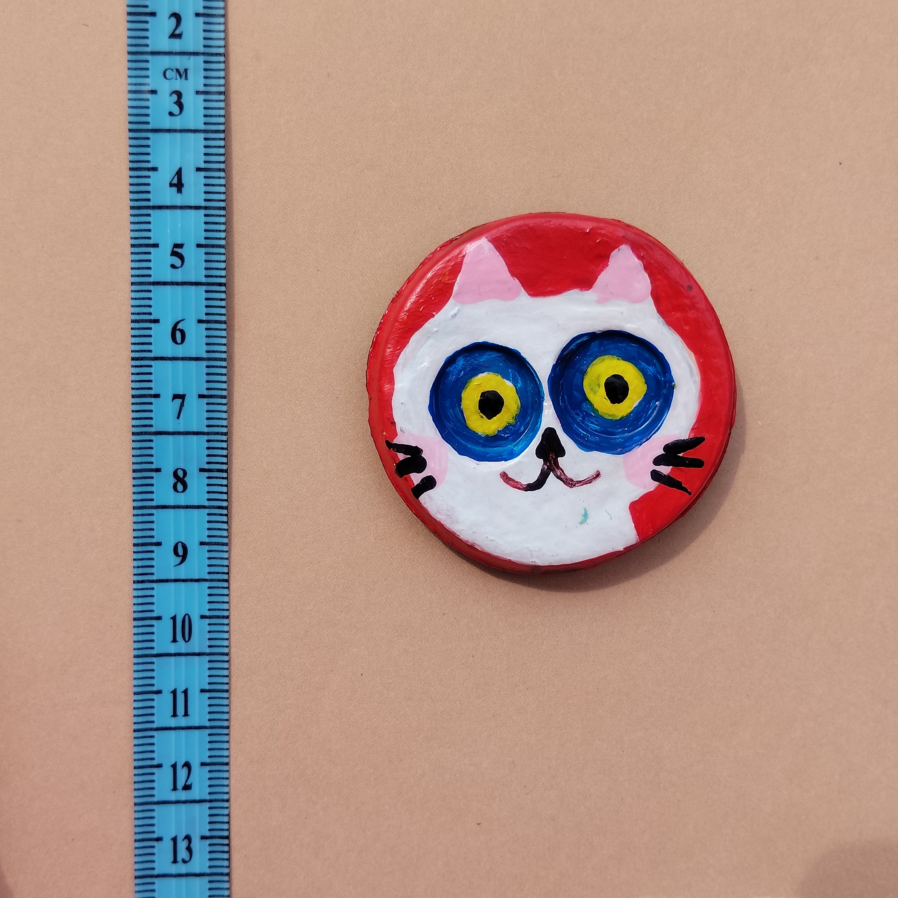 Round magnet with cat face design lying on beige background with bue measuring ruler - Sustainable Home Decor & Upcycled Glass