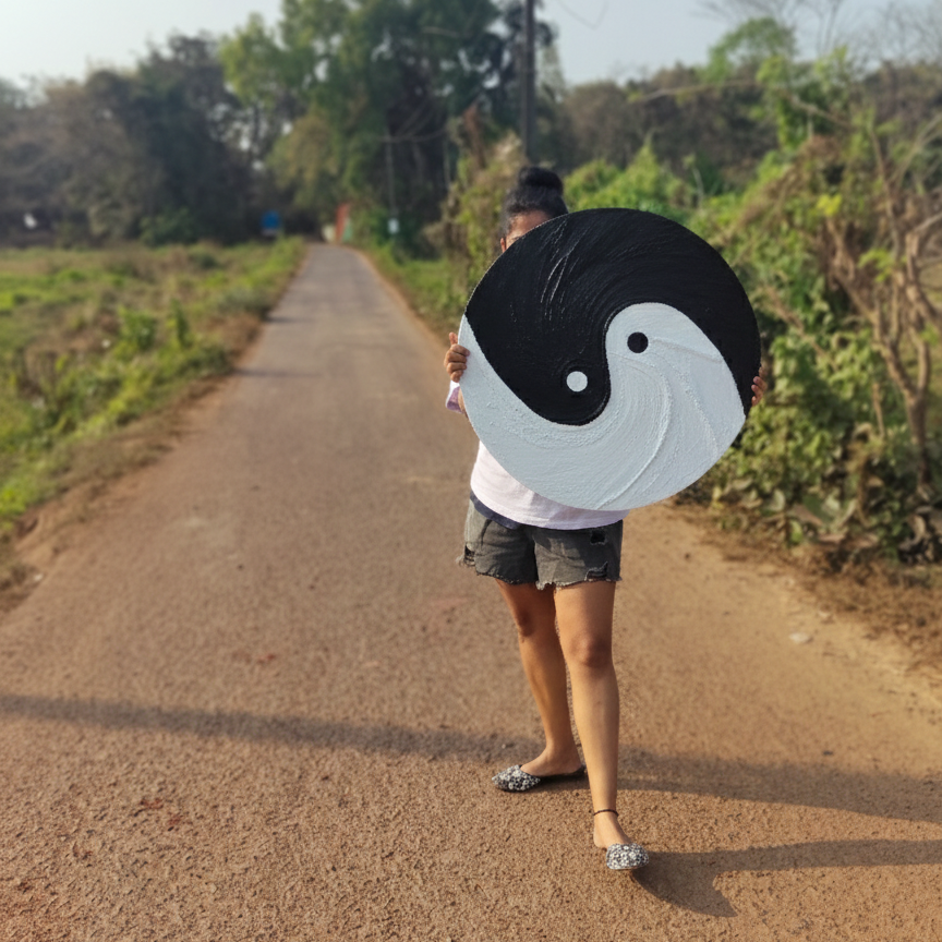 Person holding a large circular artwork with a black and white yin yang design on a road.