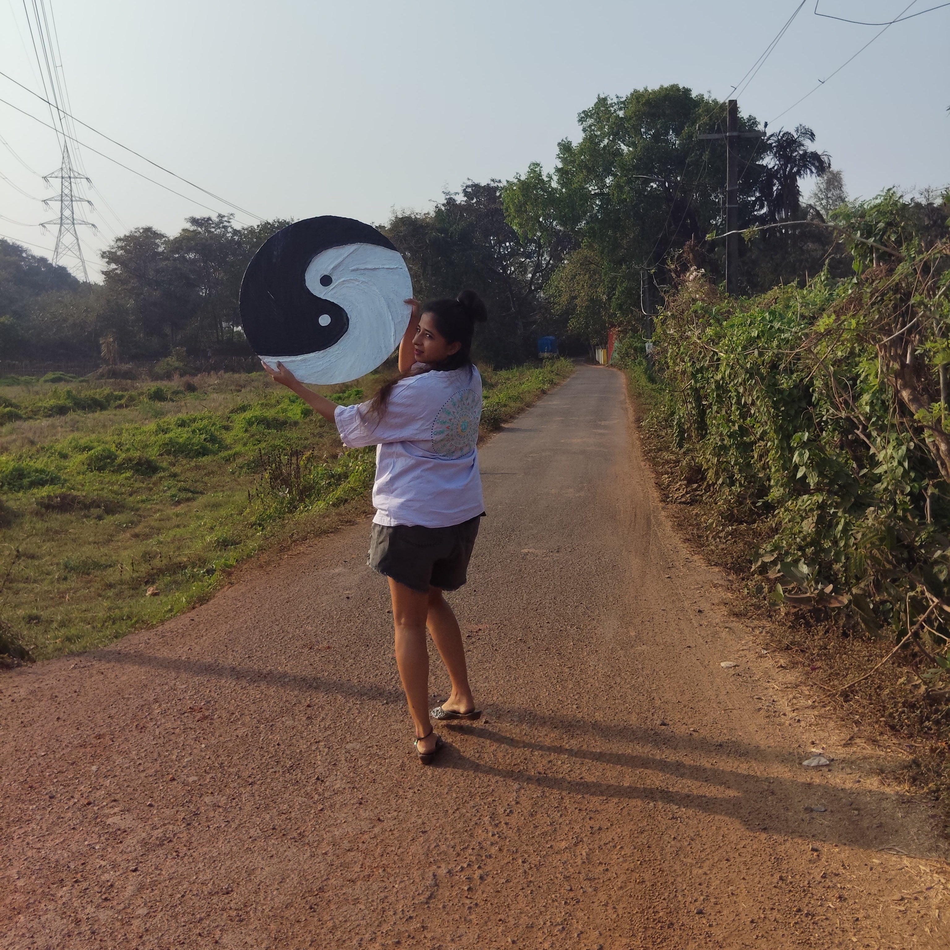 Person holding a hand textured artistic black and white yin yang symbol on a rural road.