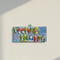 Colorful ceramic wall decor art with 'Feeling Healing' text  hanged on a light background wall